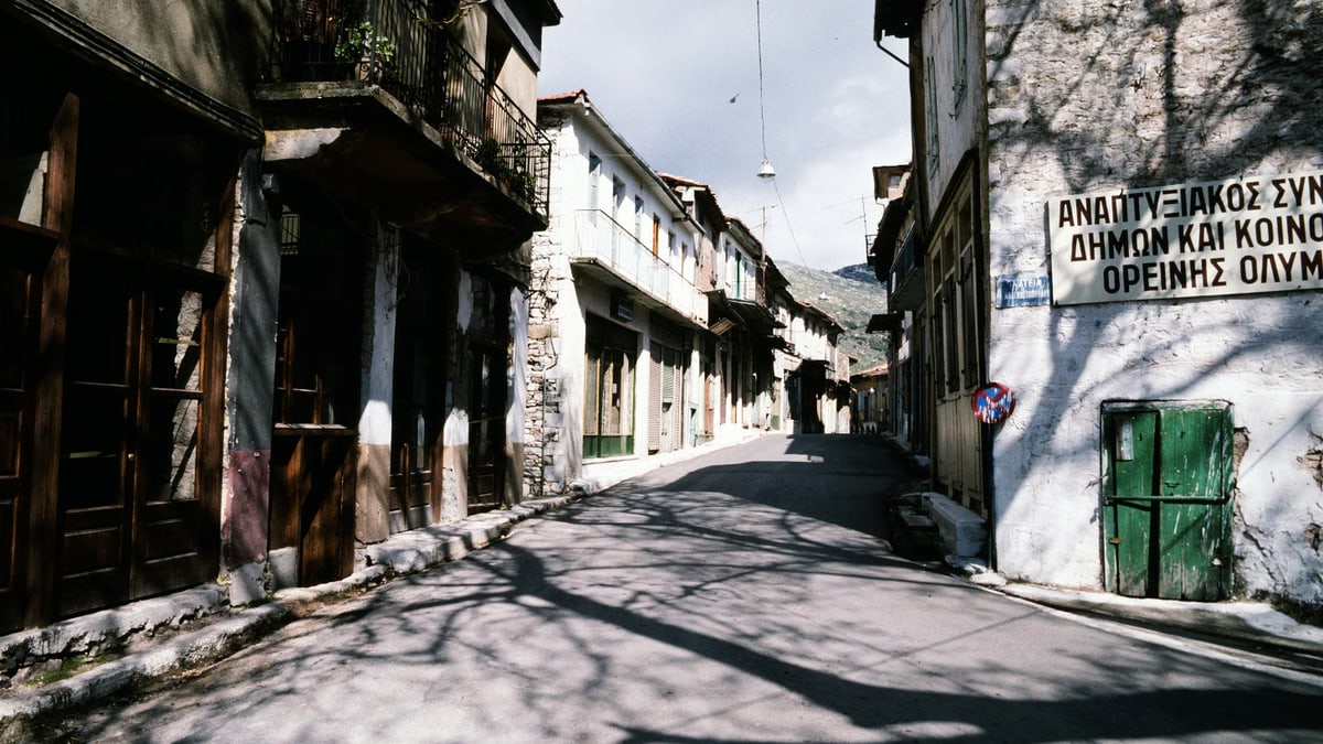 Charming sunlit street in a traditional Greek village with rustic architecture and shadows.